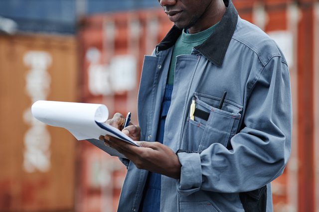 Man wearing hardhat and holding clipboard at shipping docks